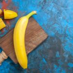 Overhead view of natural grown fresh banan on wooden cutting board on blue background