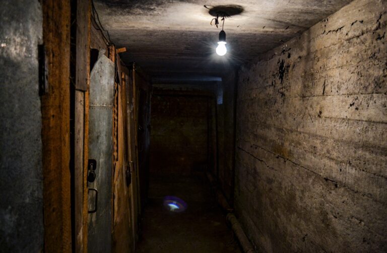 A terrible dark concrete corridor in the basement with locked doors, lit by a single light bulb